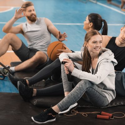 Smiling young sporty people sitting on mats and talking in sports hall Smiling young sporty people sitting on mats and talking in sports hall